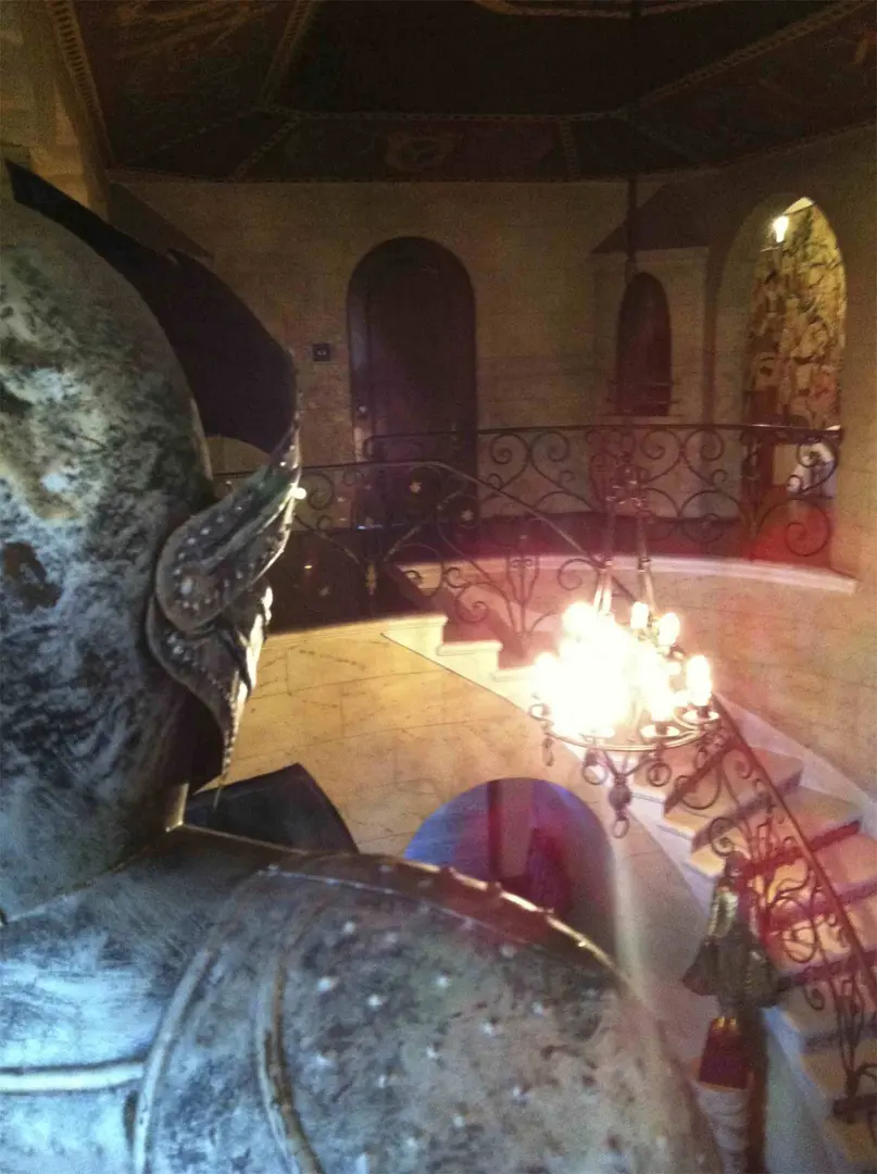 Statue overlooking a grand staircase with a chandelier in an ornate interior.