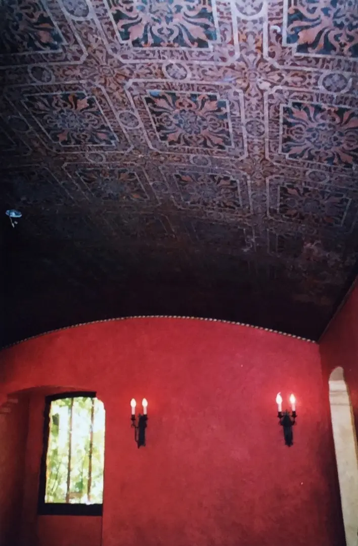Ornate ceiling with intricate designs above red walls and candle sconces.