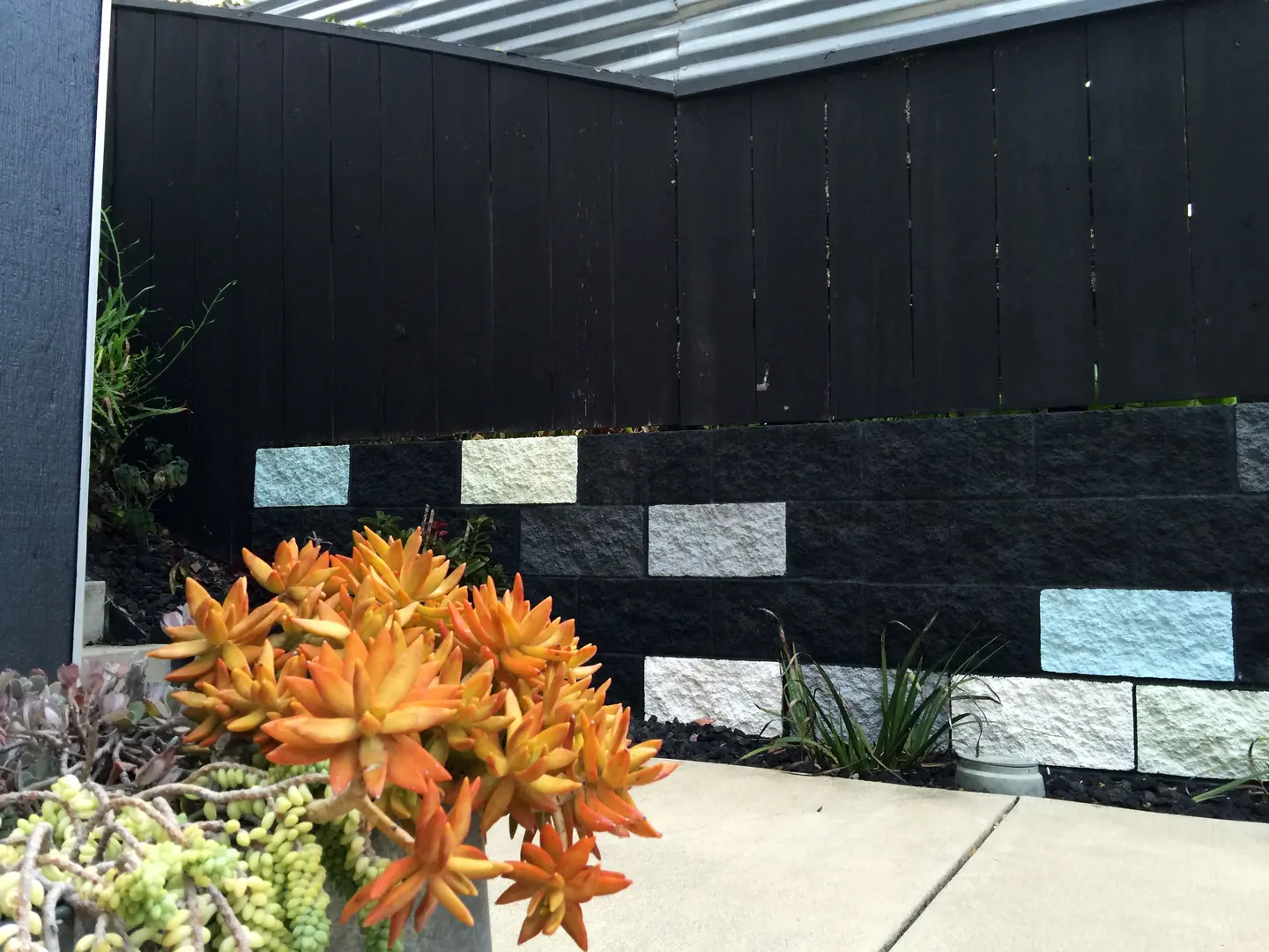 Modern black wall with colorful stone accents and orange flowers in front.