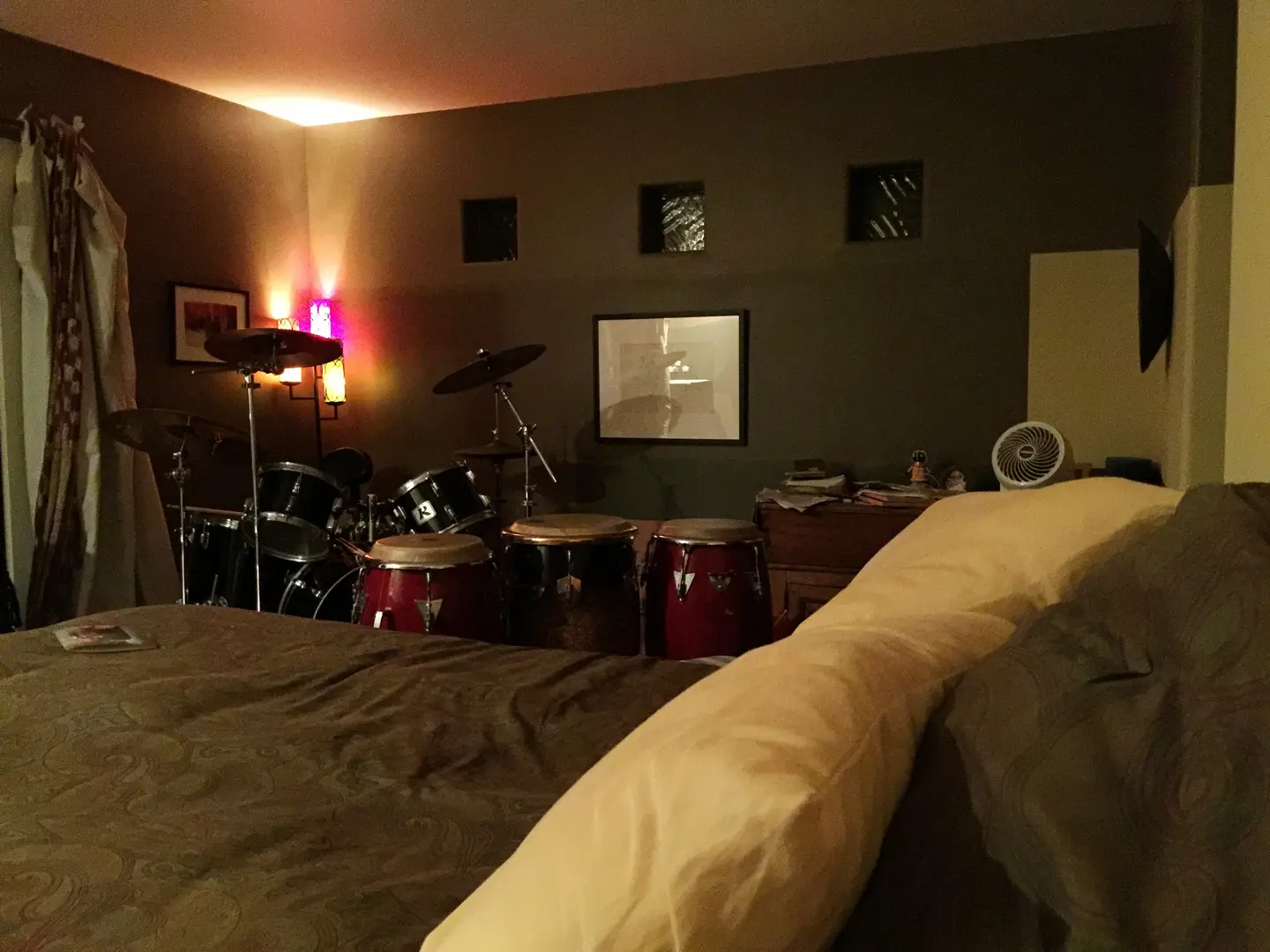 Cozy room with drums, soft lighting, and a bed.