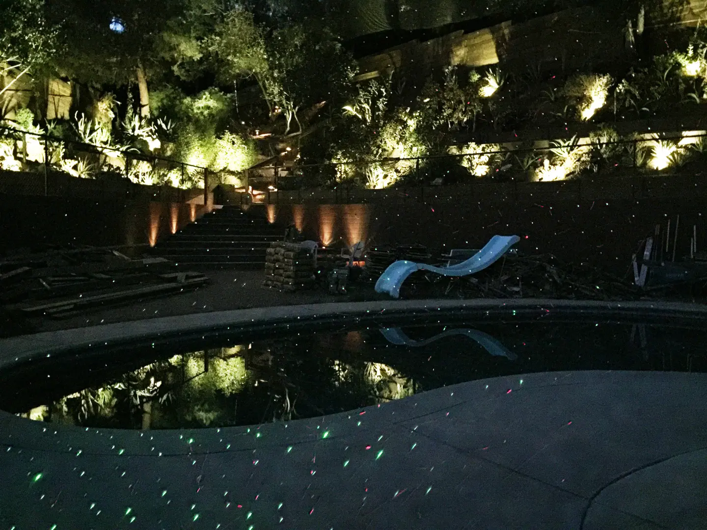 Night view of a cozy backyard pool with ambient lighting and a slide.