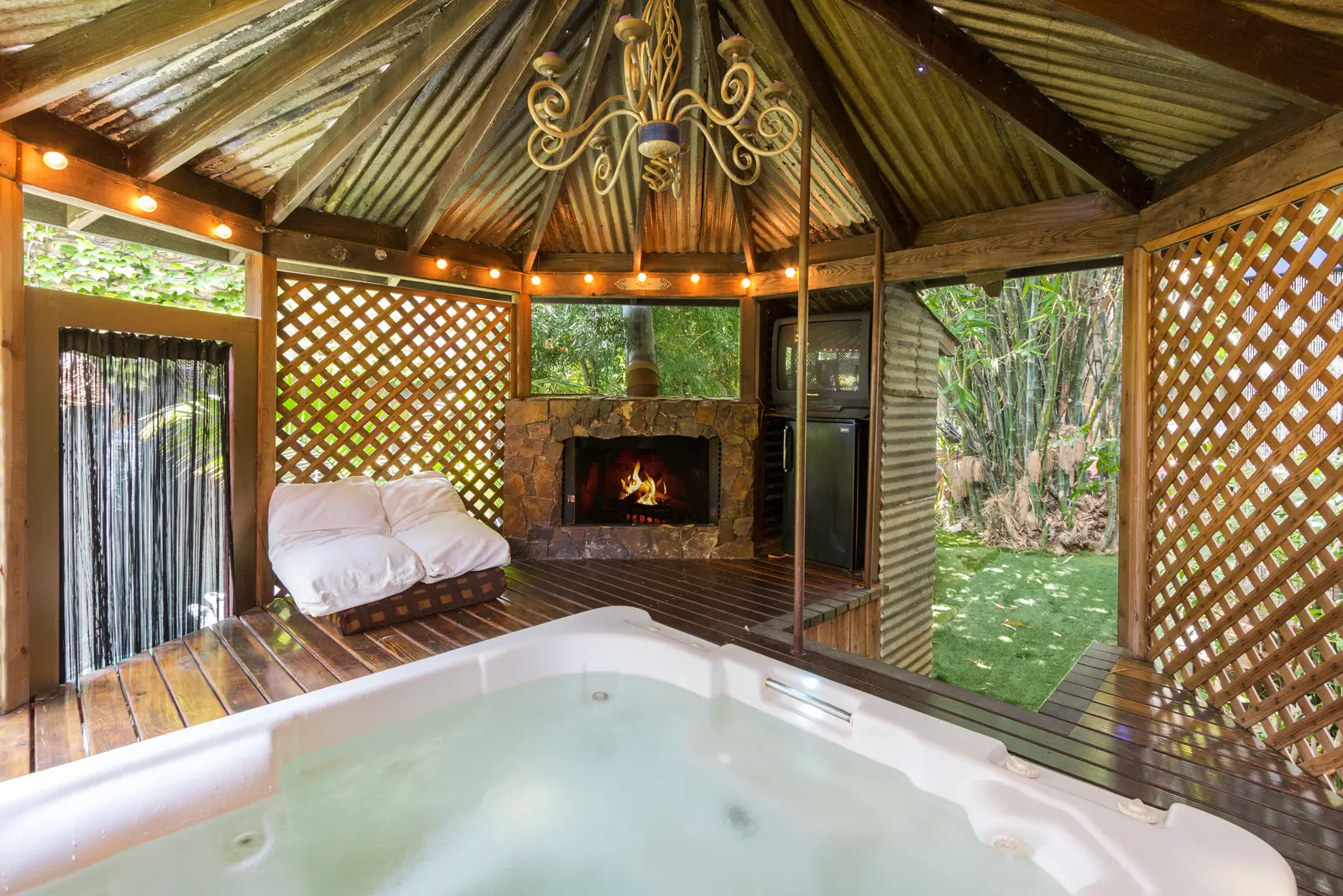 Cozy outdoor gazebo with a fireplace and hot tub surrounded by greenery.