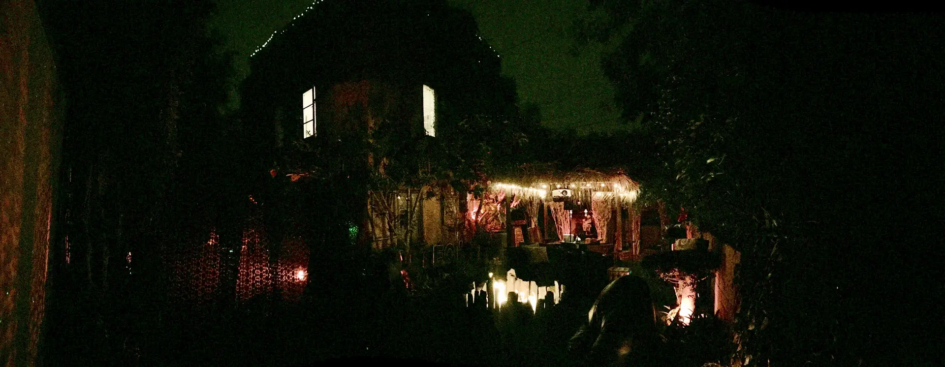A cozy house with string lights reflecting on water at night.
