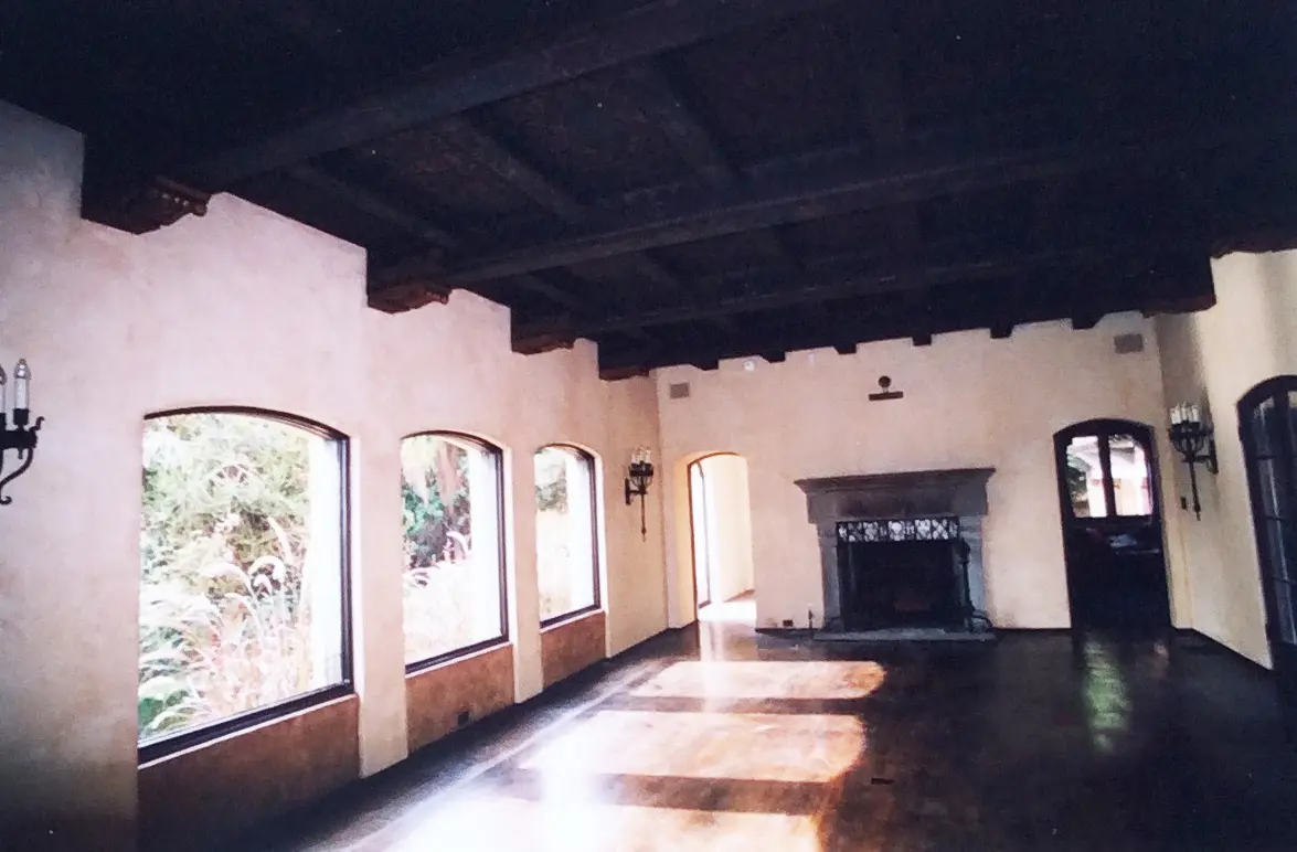 Empty room with wooden ceiling beams and arched windows.